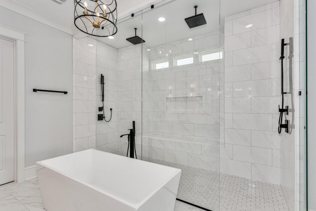 A freestanding white bathtub with a glass shower behind it featuring two shower heads.